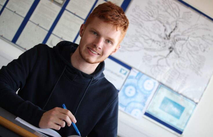 Student sitting at a desk holding a pen and smiling