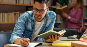Student in a library making notes and reading